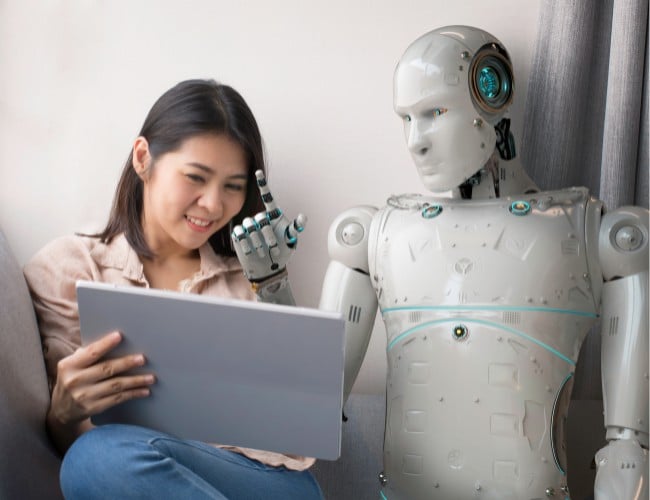 a women and a robot sitting and discussing something on a large tablet